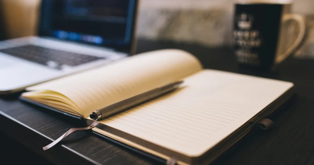 Un carnet et un stylo sur un bureau de travail, en illustration de la définition SEO de Élagage de contenu