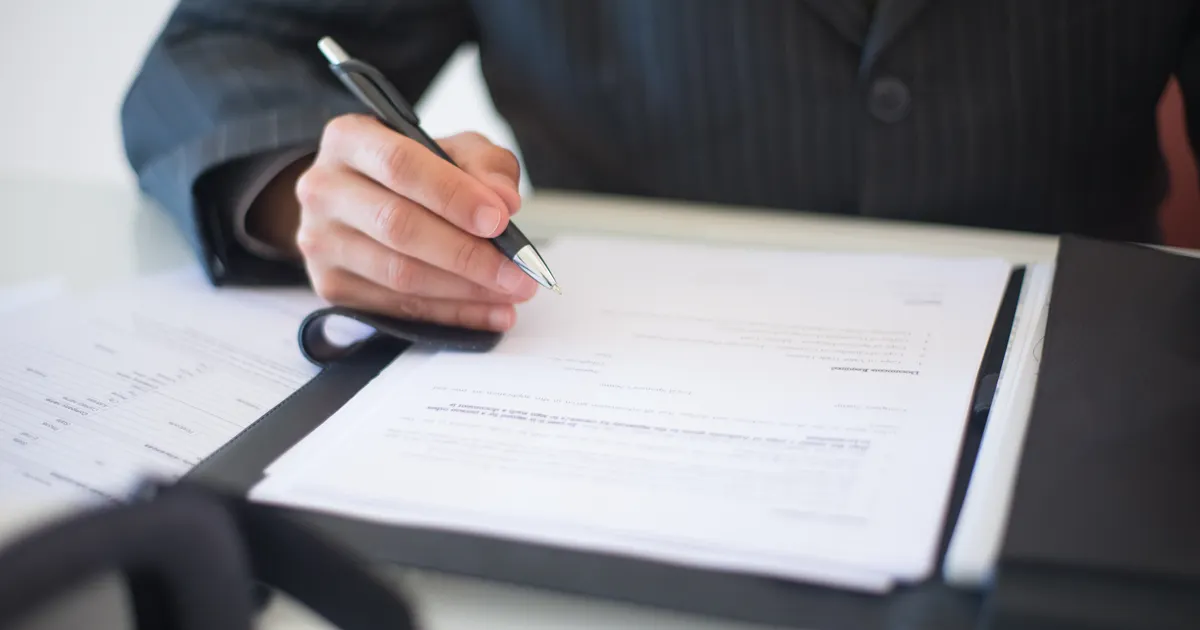 Close-up of a hand signing documents with a pen, symbolizing an important business contract, illustrating the Trust Agency legal notice